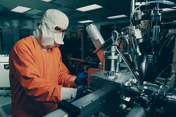 A researcher in cleanroom garments operating deposition equipment inside the Birck cleanroom.